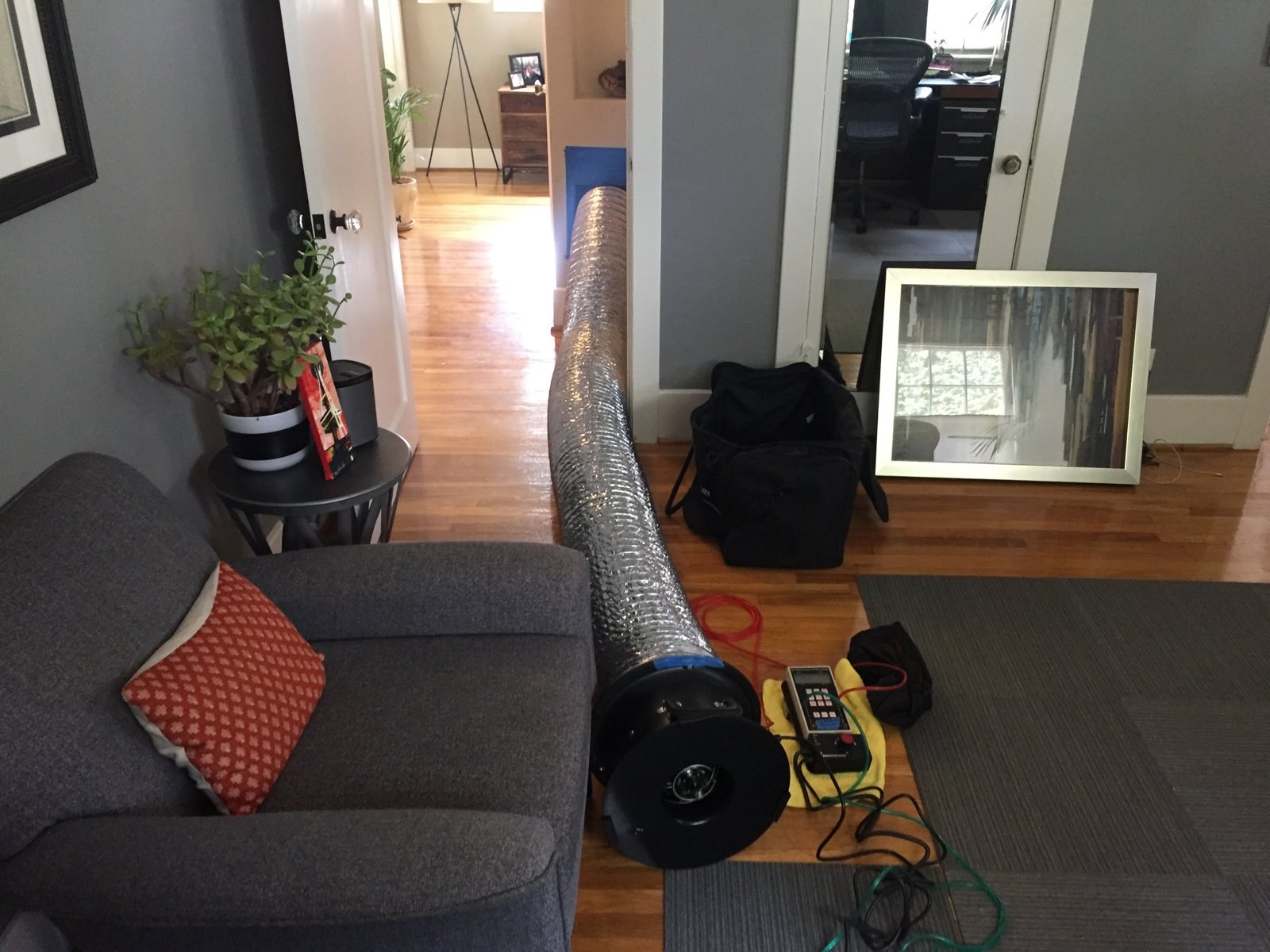 A duct leakage test set up in a living room: the fan connects to the system and the gauge reads the pressure. This is the kind of testing California's HERS rules made routine.